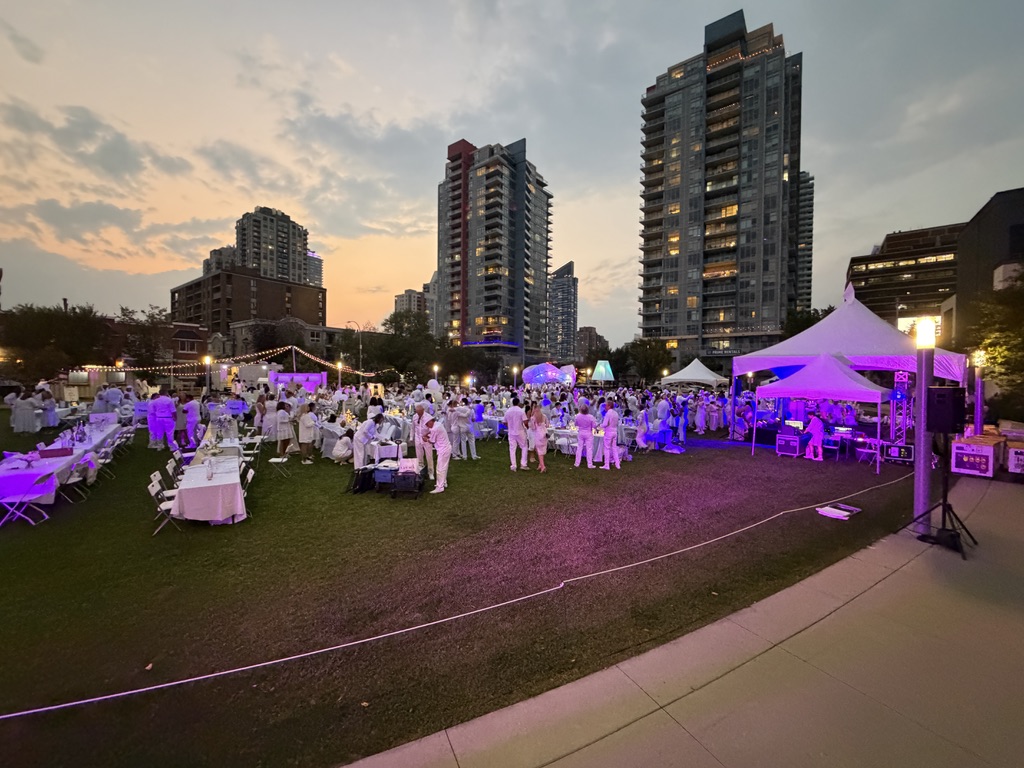 Outdoor Dinner en Blanc event at dusk with lit tents and city skyline