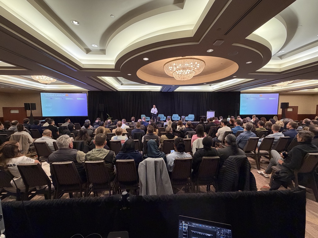 Full town hall audience facing a presenter and twin screens